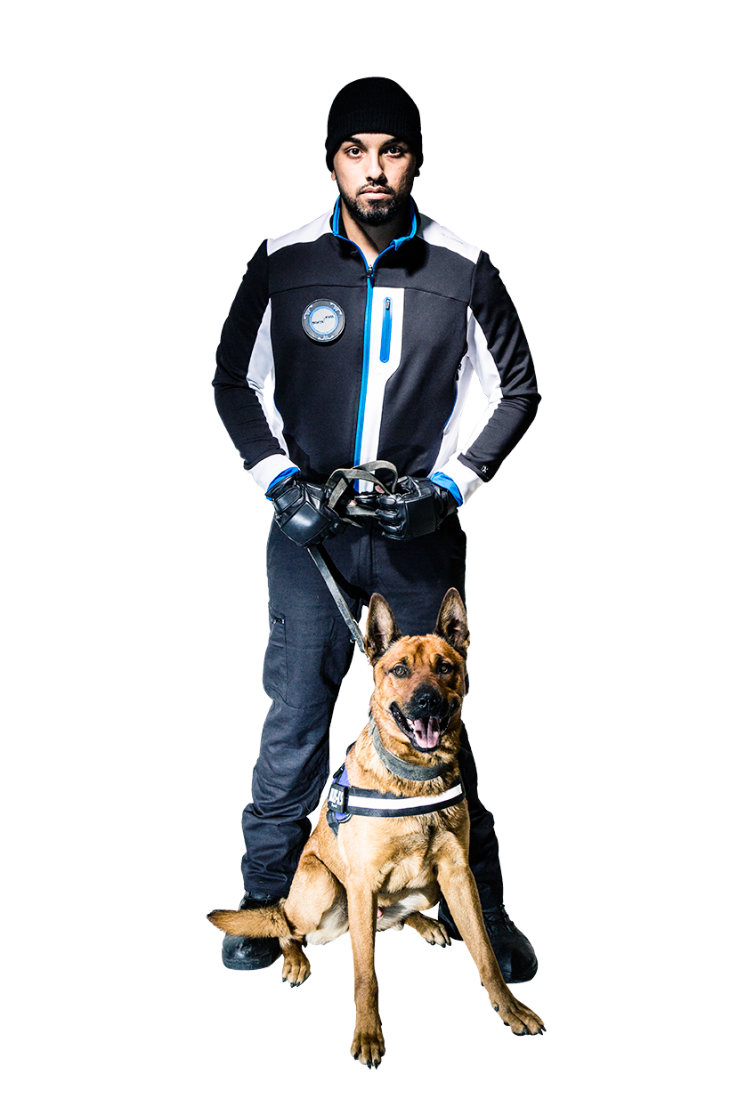 Un agent cynophile en tenue noire tient en laisse un chien assis de race malinois de couleur fauve avec la gueule ouverte.